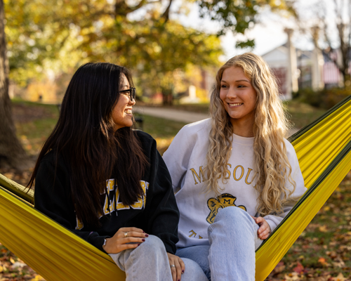 Student smiling and sitting on a hammock.