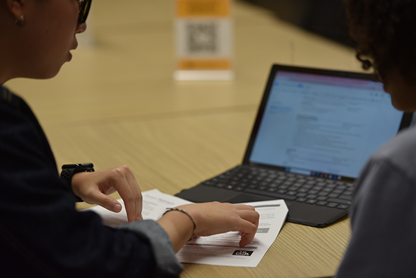 Computer with student point to a sheet of paper with the browser open.