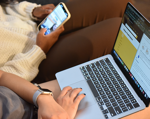 Overhead view of a student on computer browsing website and another student browsing their cellphone