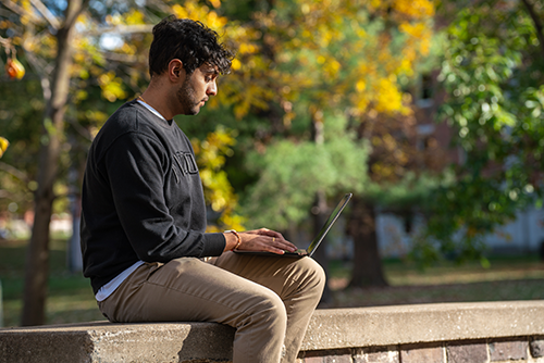 Student working on computer sitting outside.