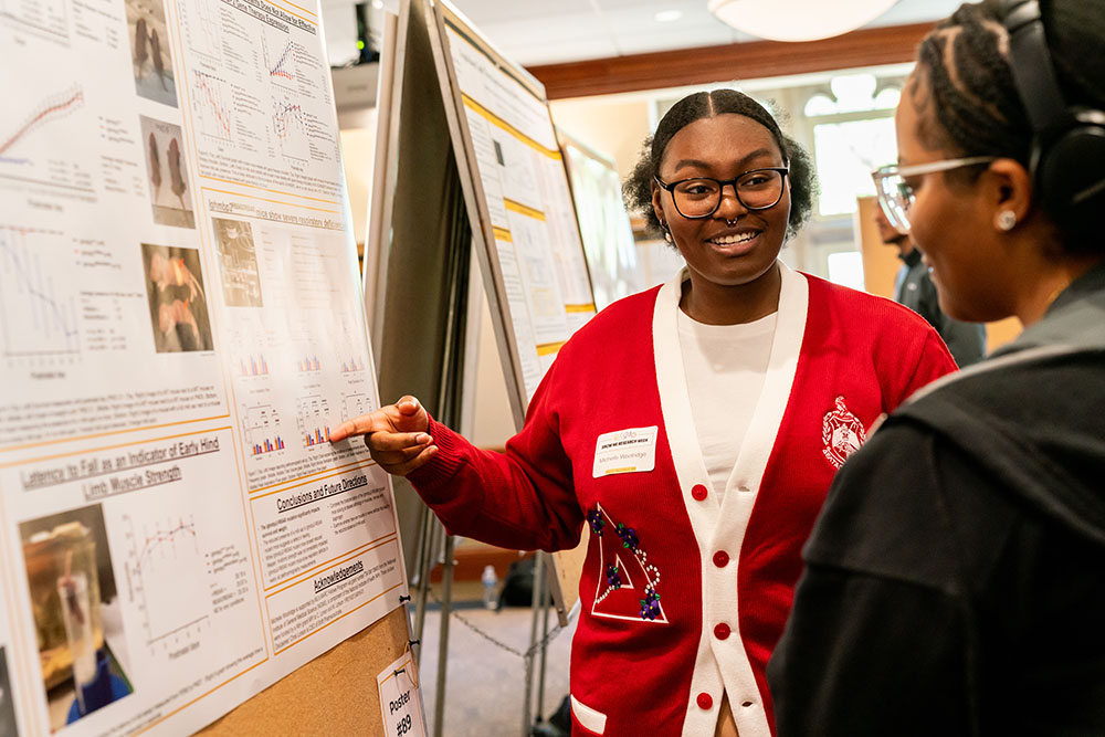 Student presenting her research poster to a friend.