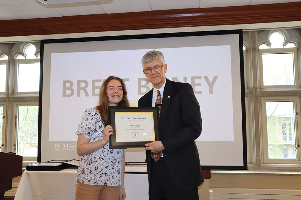 Brett Boney holding certificate at awards ceremony with Dr. Spain.