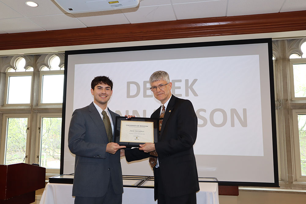 Derek Dannaldson holding certificate at awards ceremony with Dr. Spain.