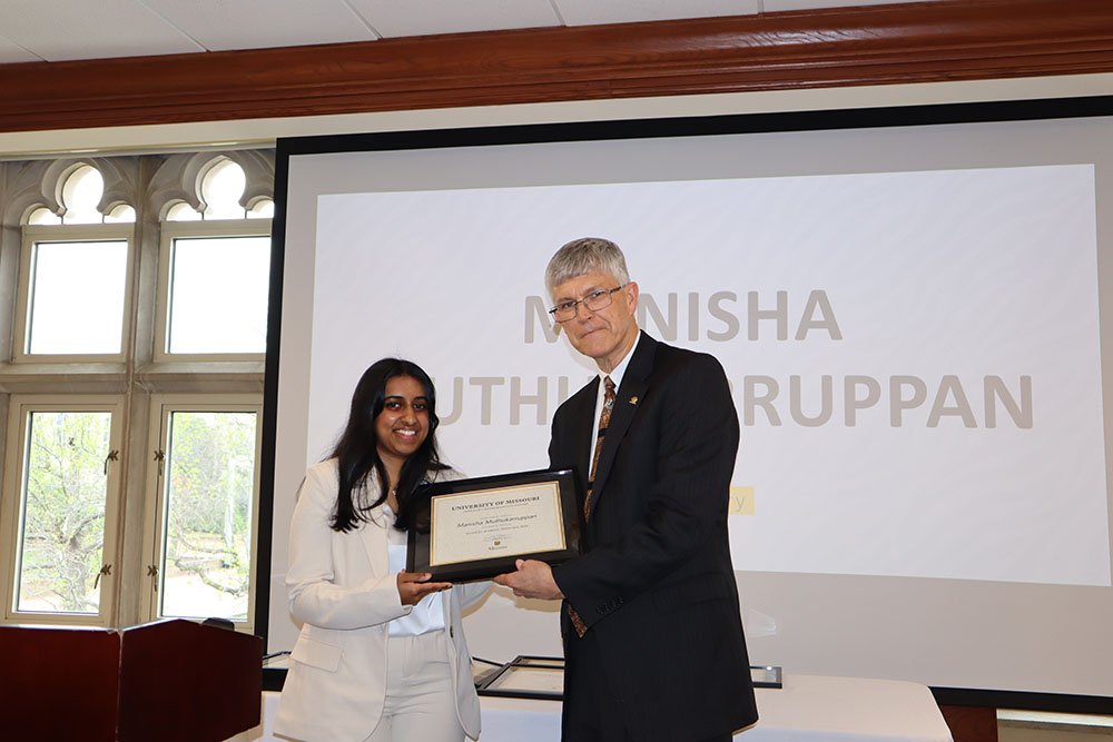 Manisha Muthukaruppan holding certificate at awards ceremony with Dr. Spain.