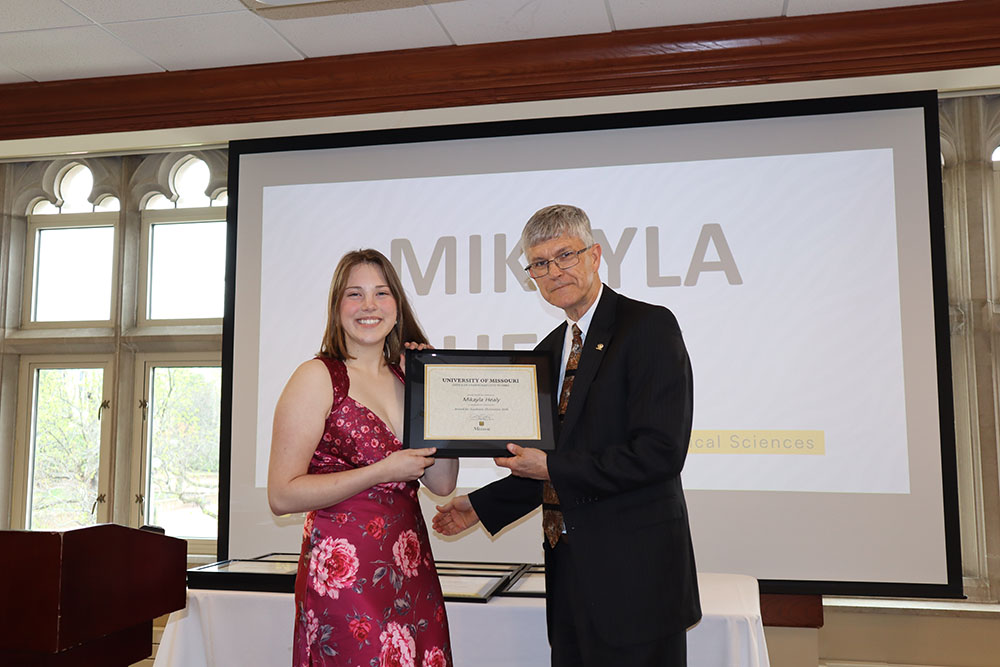Mikayla Healy holding certificate at awards ceremony with Dr. Spain.