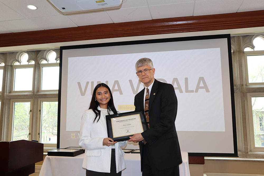 Vina Vedala holding certificate at awards ceremony with Dr. Spain.